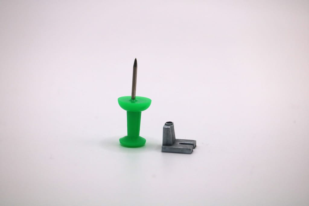 Microcomponente zama con puntina verde accanto per scala dimensionale, piccolo pezzo tecnico grigio. - Micrometal